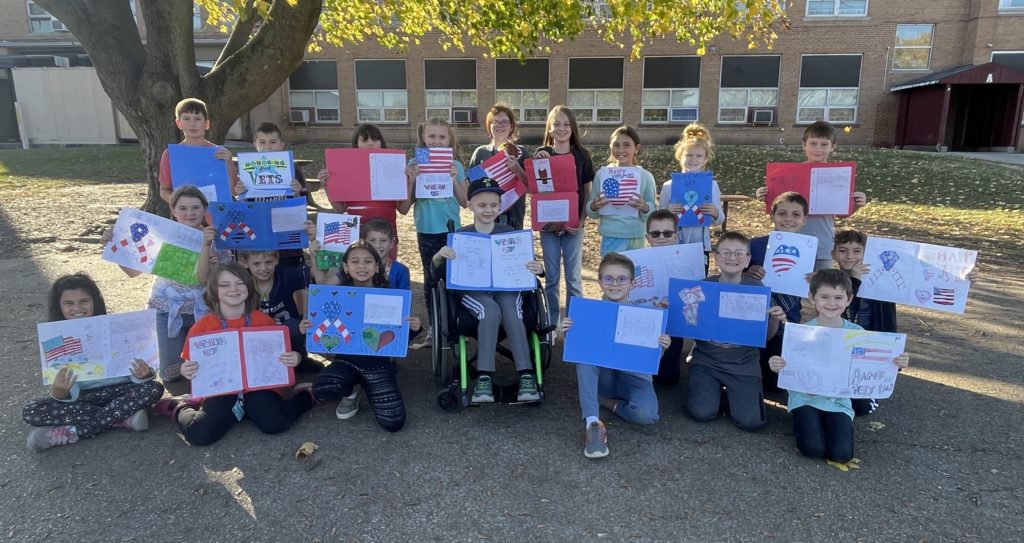 4th Grade Class outside group photo holding their handmade cards for veterans.